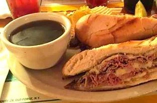 The French dip on a diner plate — sliced top round and melted provolone on garlic-grilled french bread, with a cup of au jus and a pickle spear